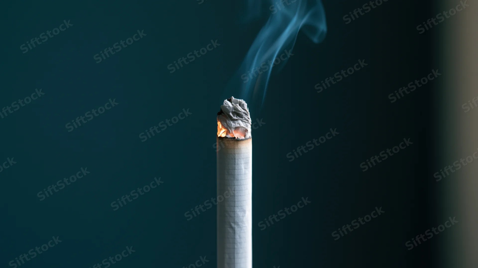 Lit cigarette with glowing ember and rising smoke against dark blue background