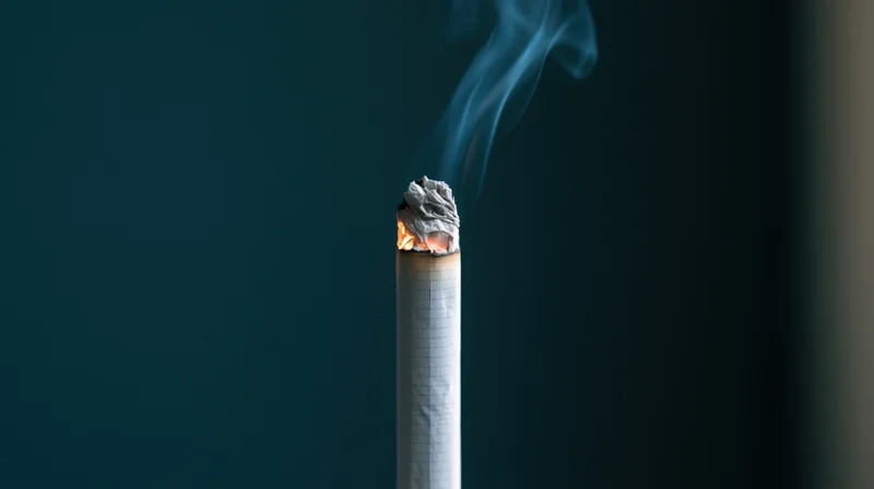Lit cigarette with glowing ember and rising smoke against dark blue background