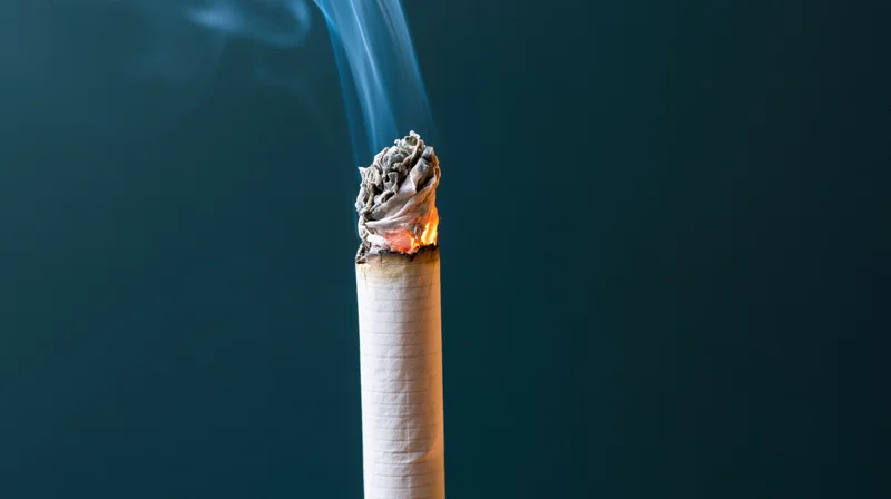 Lit cigarette burning upright with glowing ember and rising smoke against dark background