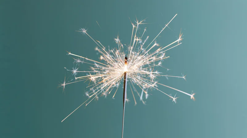 Lit sparkler radiating white sparks against teal background