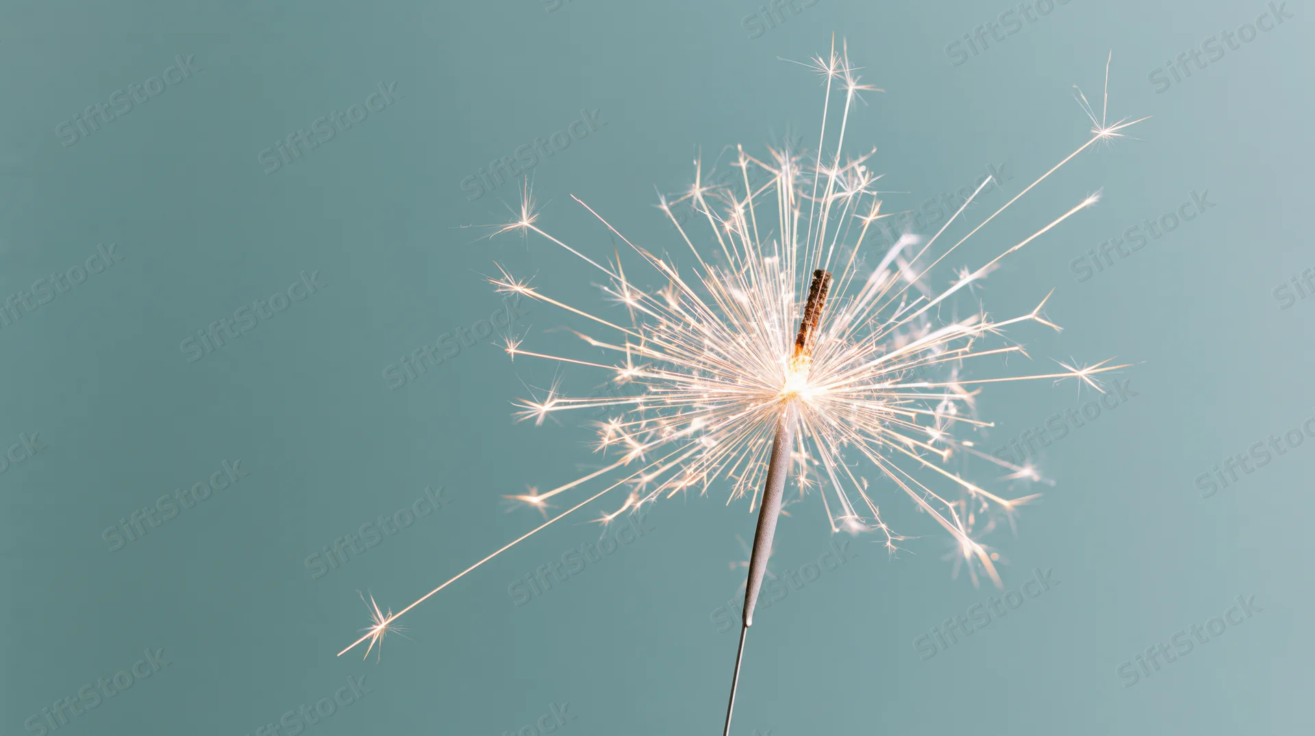 Lit sparkler radiating white sparks against teal background