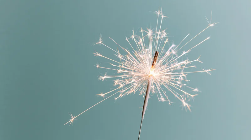 Lit sparkler radiating white sparks against teal background