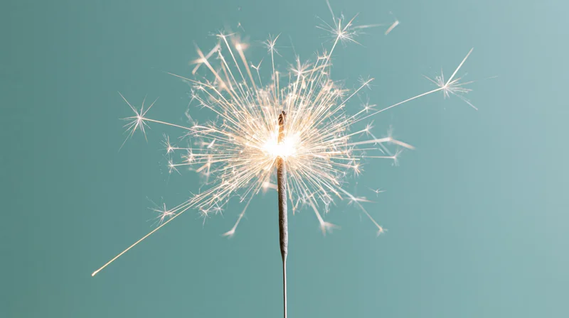 Lit sparkler radiating white sparks against teal background