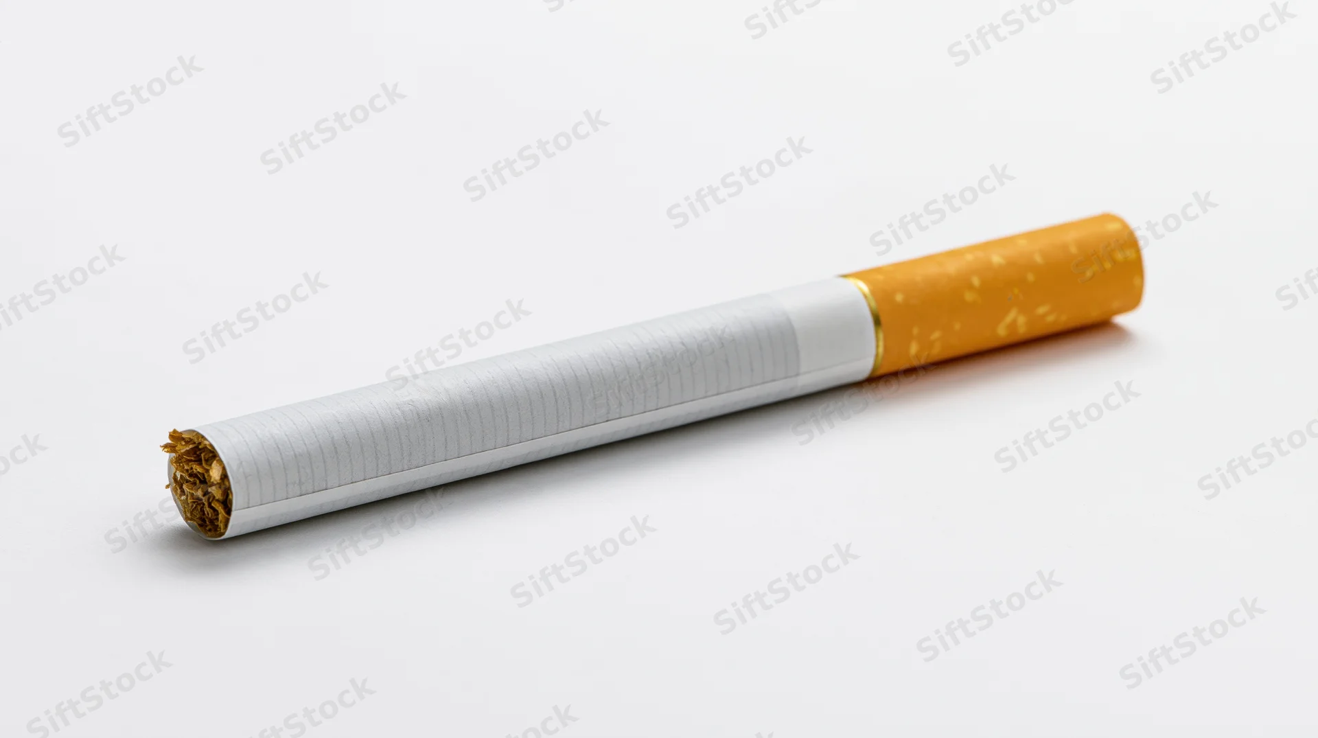 Unlit cigarette with orange filter lying diagonally on white background