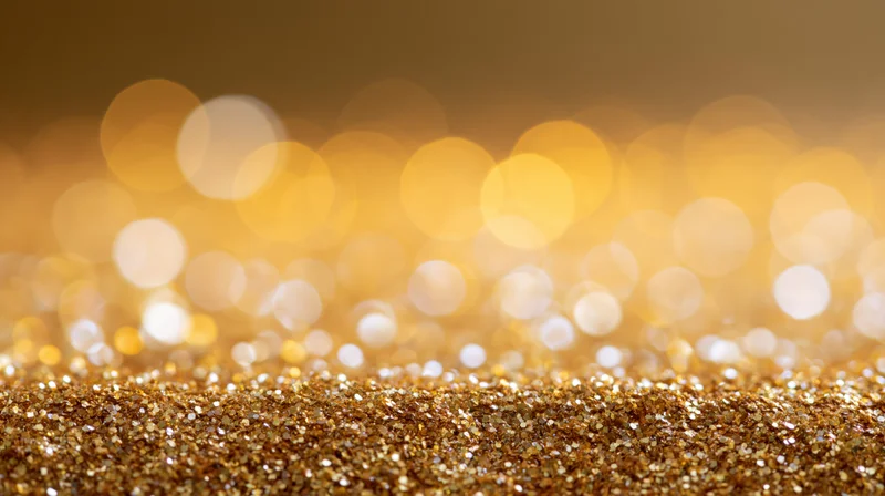 Gold glitter particles scattered across a surface with blurred bokeh lights in the background