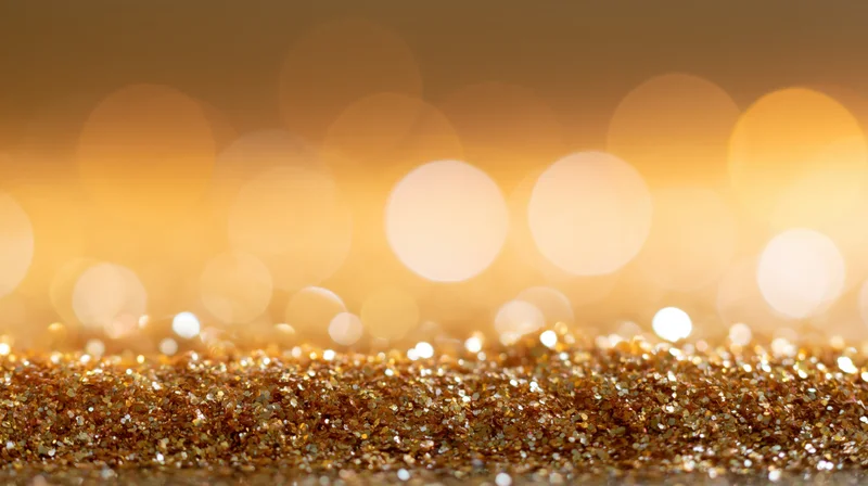 Gold glitter scattered across a surface with blurred bokeh lights in the background