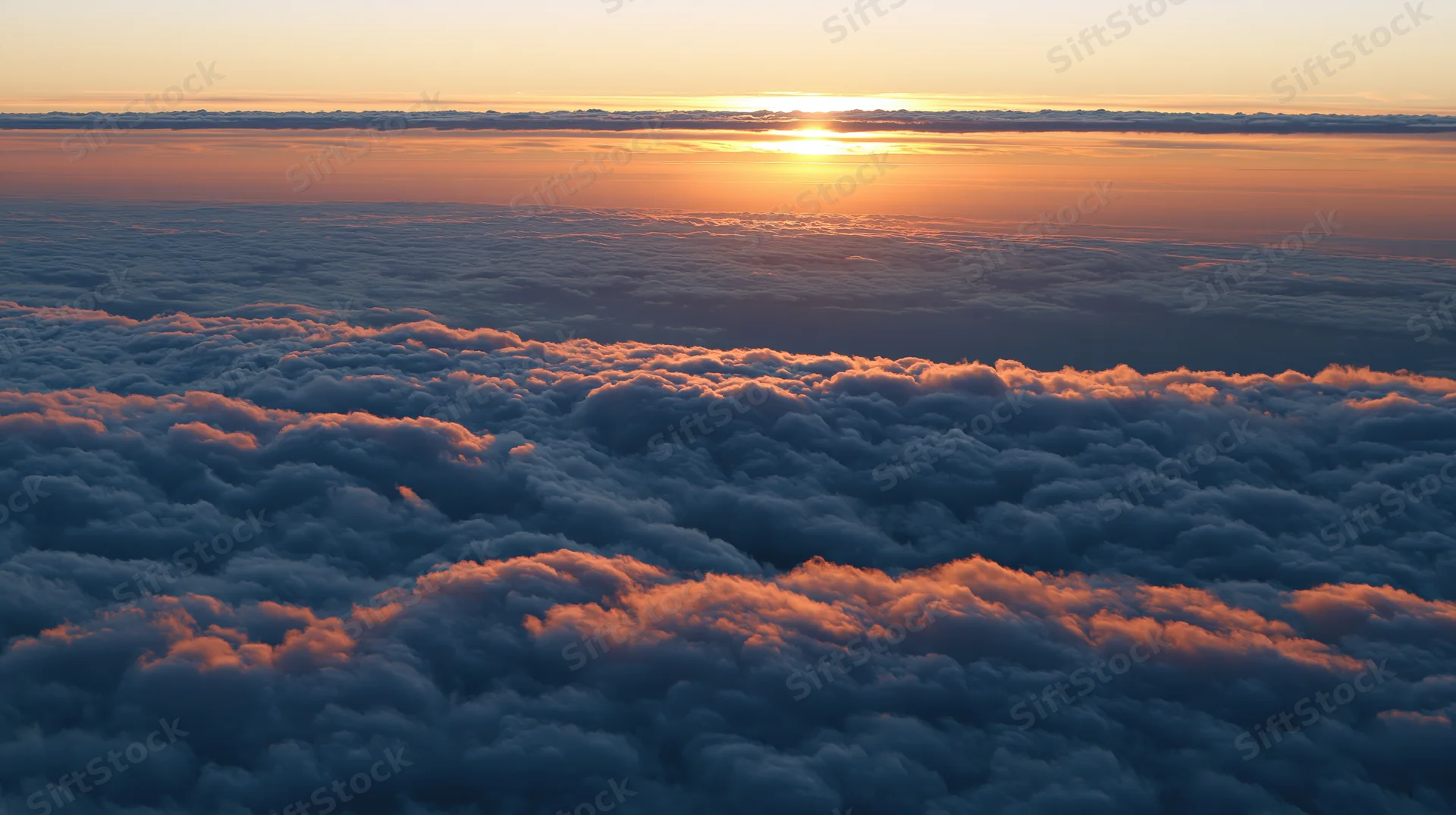 Aerial view above dense clouds at sunset with golden light on horizon