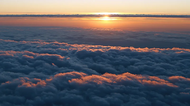 Aerial view above dense clouds at sunset with golden light on horizon