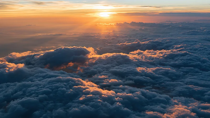 Aerial view above dense clouds at sunset with golden light and horizon in sky