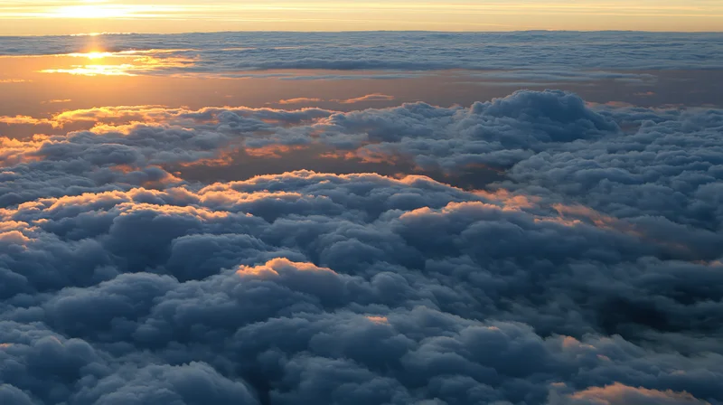 Aerial view above dense clouds at sunset with golden light on horizon