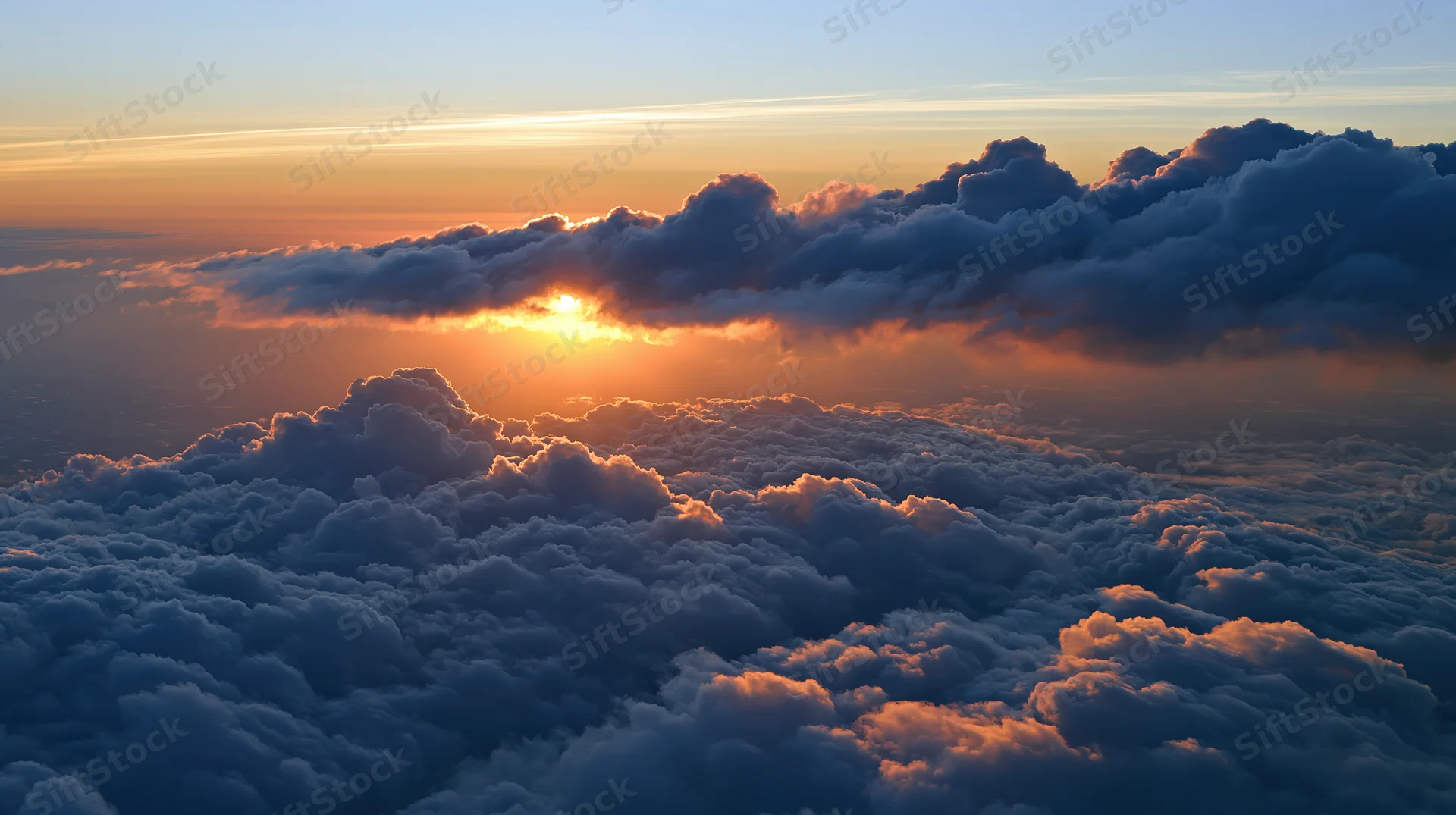Aerial view above dense clouds at sunset with sun peeking through cloud layer