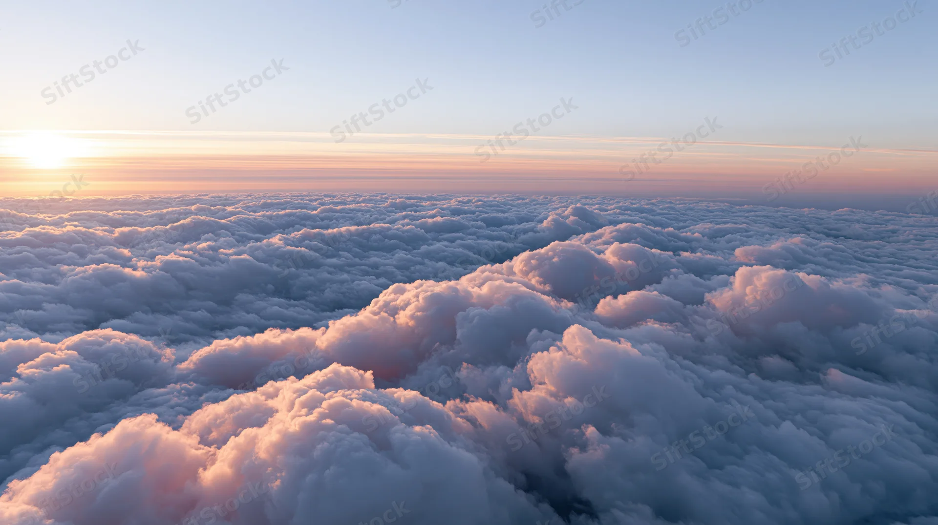 Aerial view of a sea of cumulus clouds at sunset with pink and orange hues along the horizon