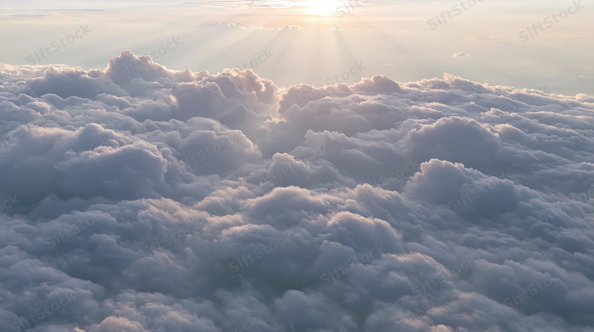 Aerial view of a vast cloudscape at sunrise with sun rays above the horizon