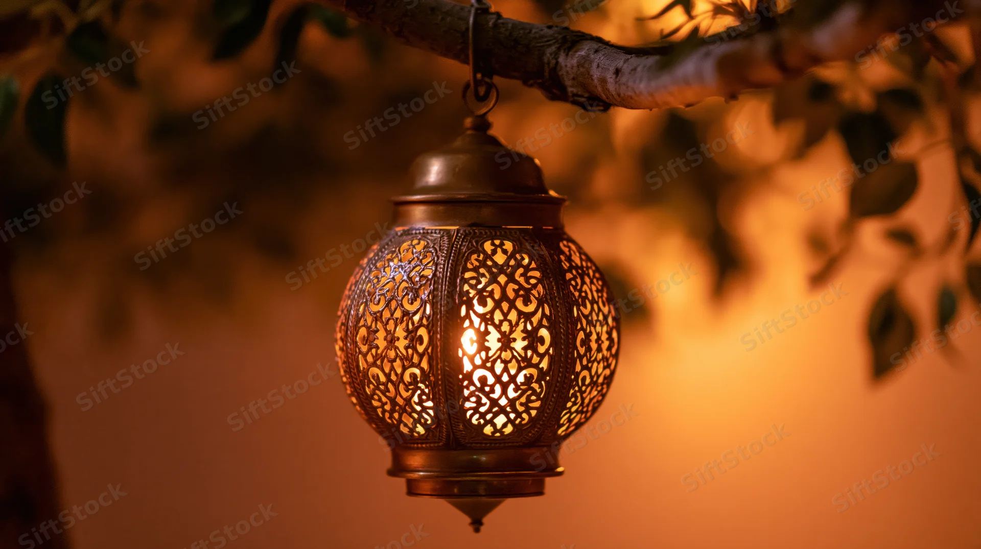 Ornate brass arabic lantern hanging from a tree branch glowing warmly at night
