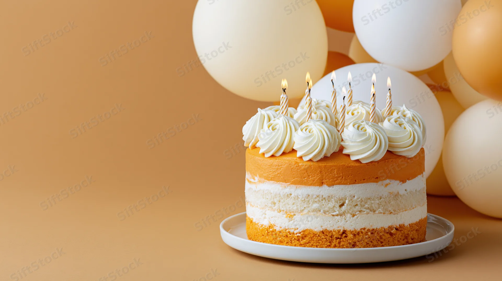 Birthday cake with lit candles on a white plate surrounded by balloons on a warm-toned background