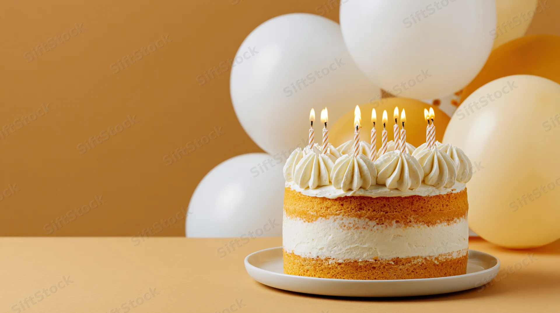 Birthday cake with lit candles on a white plate in front of balloons on a warm-toned background