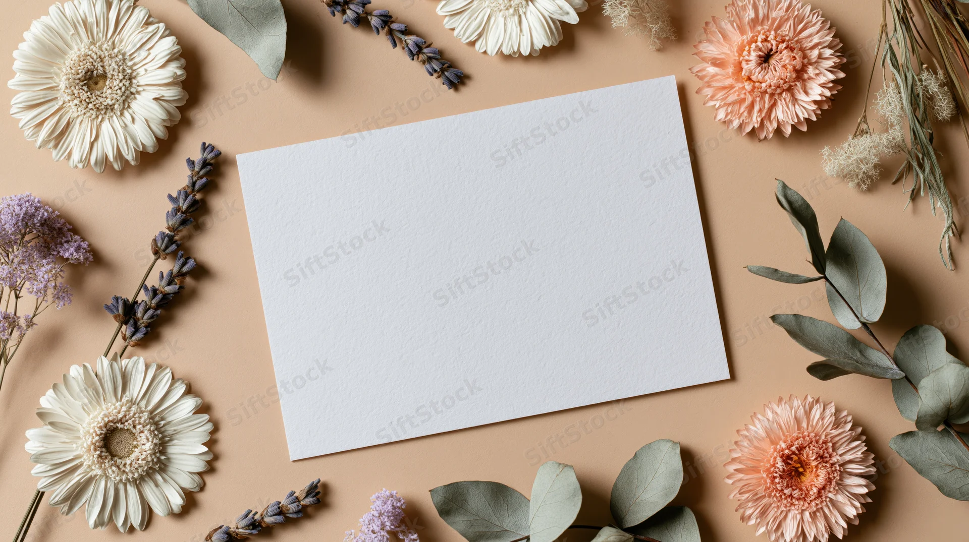 Blank white card surrounded by dried flowers and foliage on beige surface