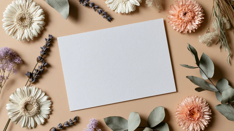 Blank white card surrounded by dried flowers and foliage on beige surface
