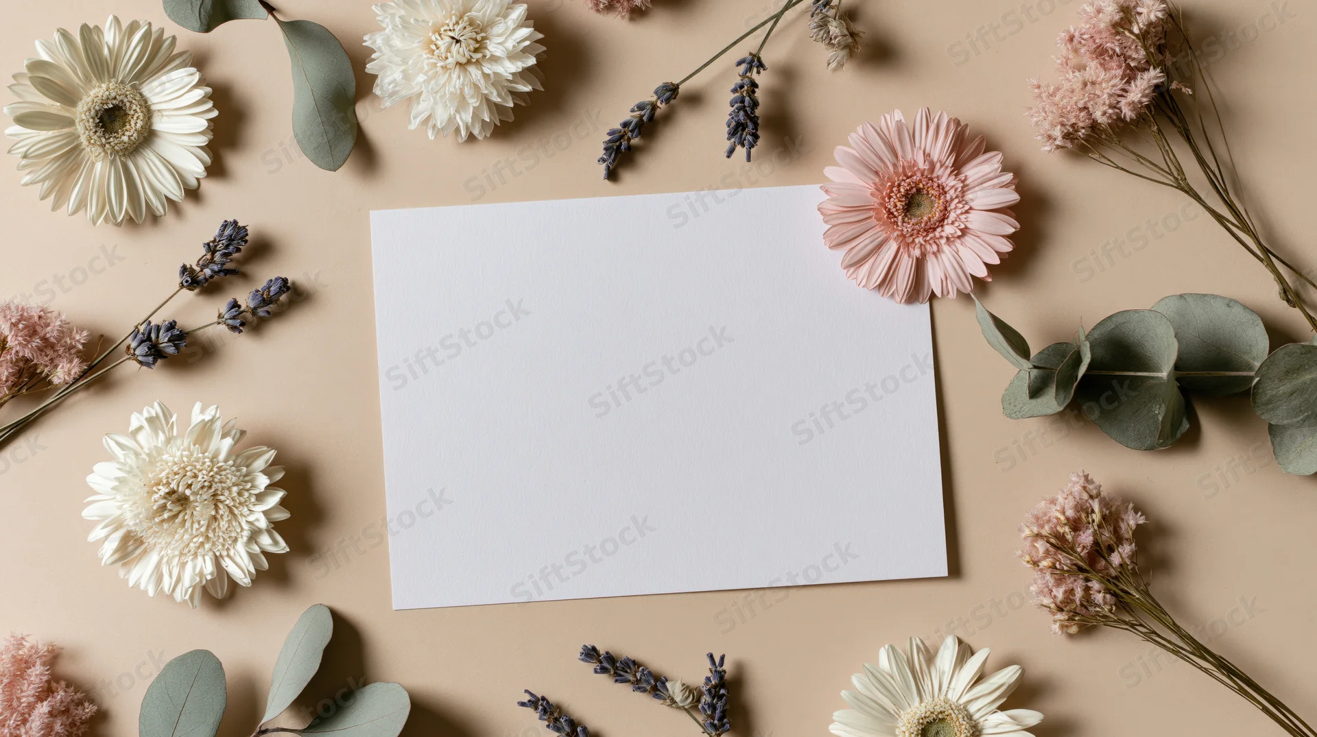 Blank white card surrounded by dried flowers and eucalyptus on beige surface