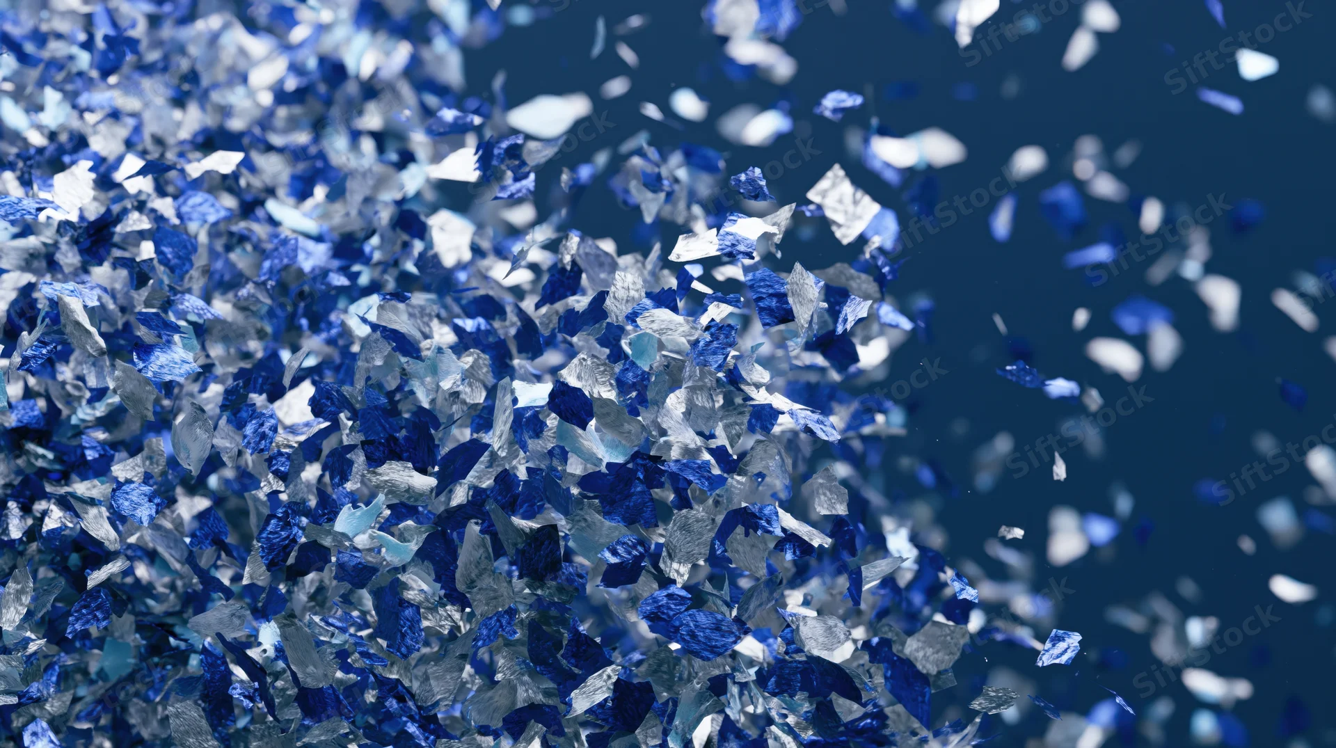 Blue and silver metallic confetti pieces falling and scattered in mid-air against a dark background