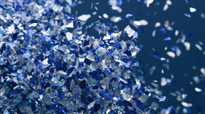 Blue and silver metallic confetti pieces falling and scattered in mid-air against a dark background