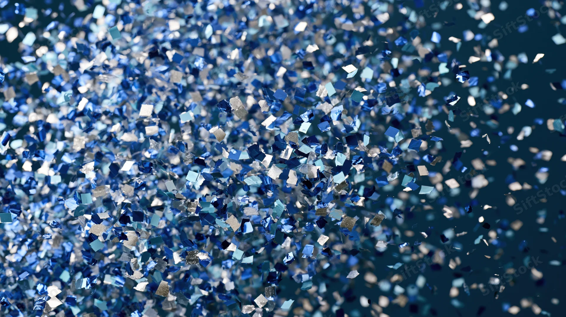 Blue and silver metallic confetti pieces falling in mid-air against a dark background