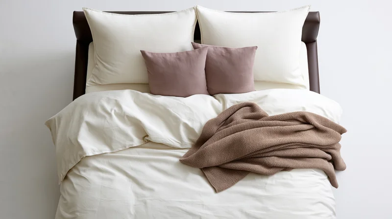 Overhead view of a double bed with white bedding and brown throw blanket on a leather frame in a minimalist bedroom