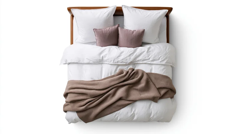 Overhead view of a double bed with white bedding and brown throw blanket on a wooden frame against white background