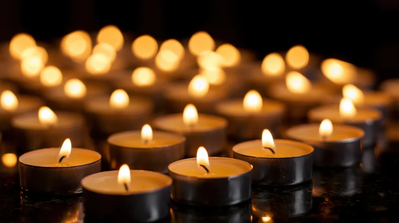 Dozens of small silver tealight candles burning on a dark reflective surface with soft glow and bokeh background