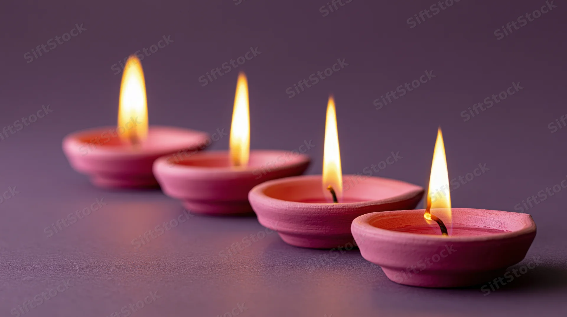 Five lit pink clay diya oil lamps arranged in diagonal row on dark surface