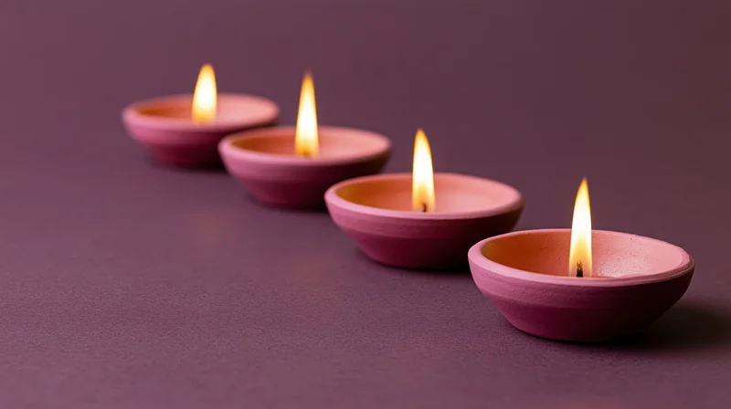 Four lit terracotta diya oil lamps arranged in diagonal row on purple surface
