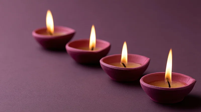 Four lit diya oil lamps arranged diagonally on a purple surface