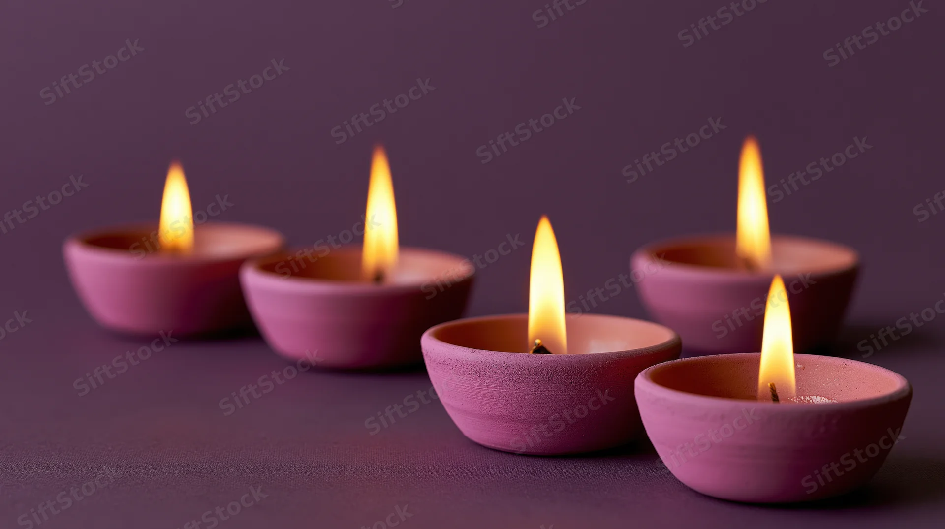 Five lit diya oil lamps arranged in diagonal row on purple surface