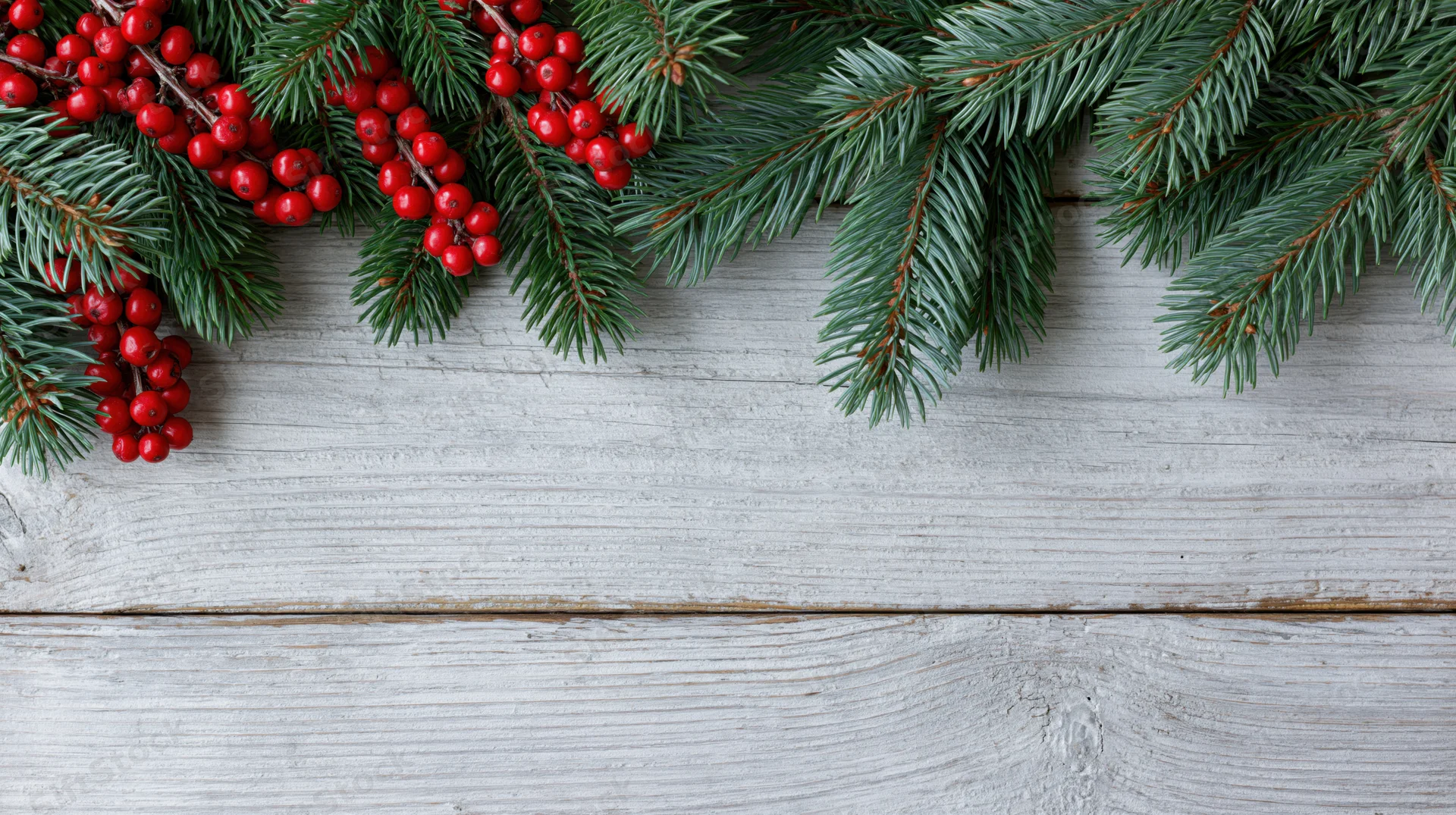 Evergreen fir branches with red berries arranged along top of white wooden surface