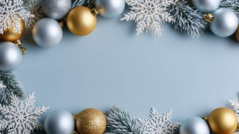 Silver and gold christmas ornaments with snowflakes and pine branches arranged in a border on a blue background with copyspace