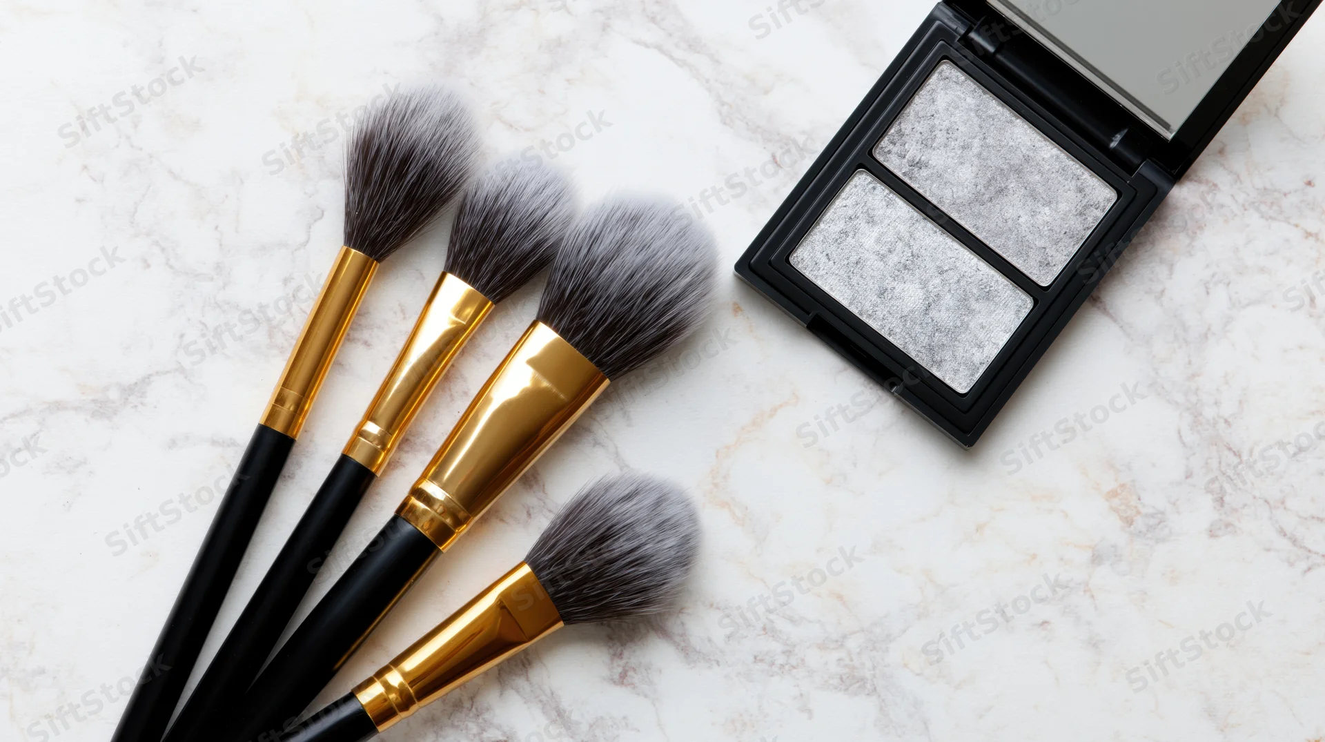 Four makeup brushes with black handles and gold ferrules arranged beside an open eyeshadow palette on a white marble surface