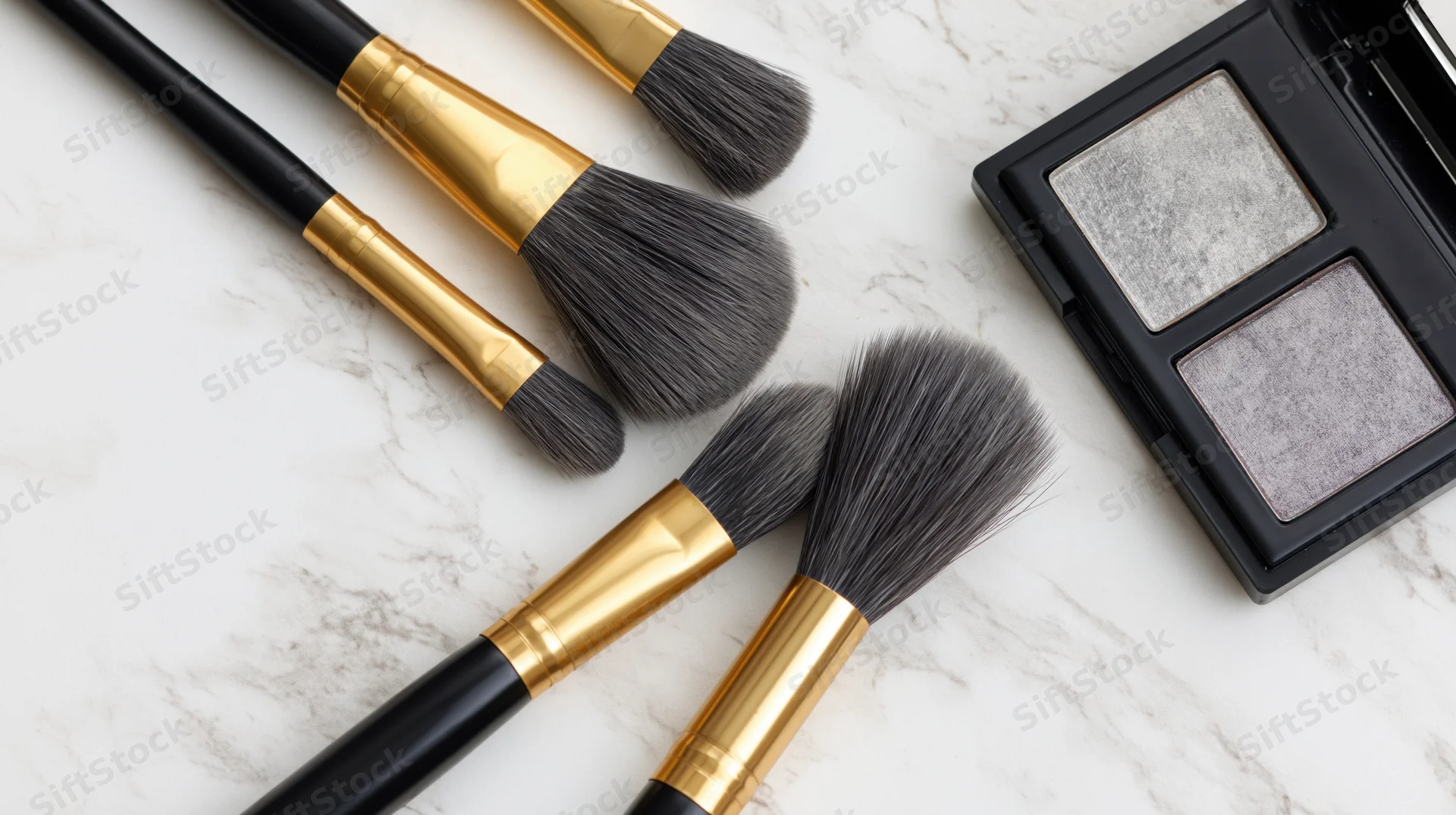 Makeup brushes with black handles and gold ferrules arranged with an eyeshadow palette on a marble surface