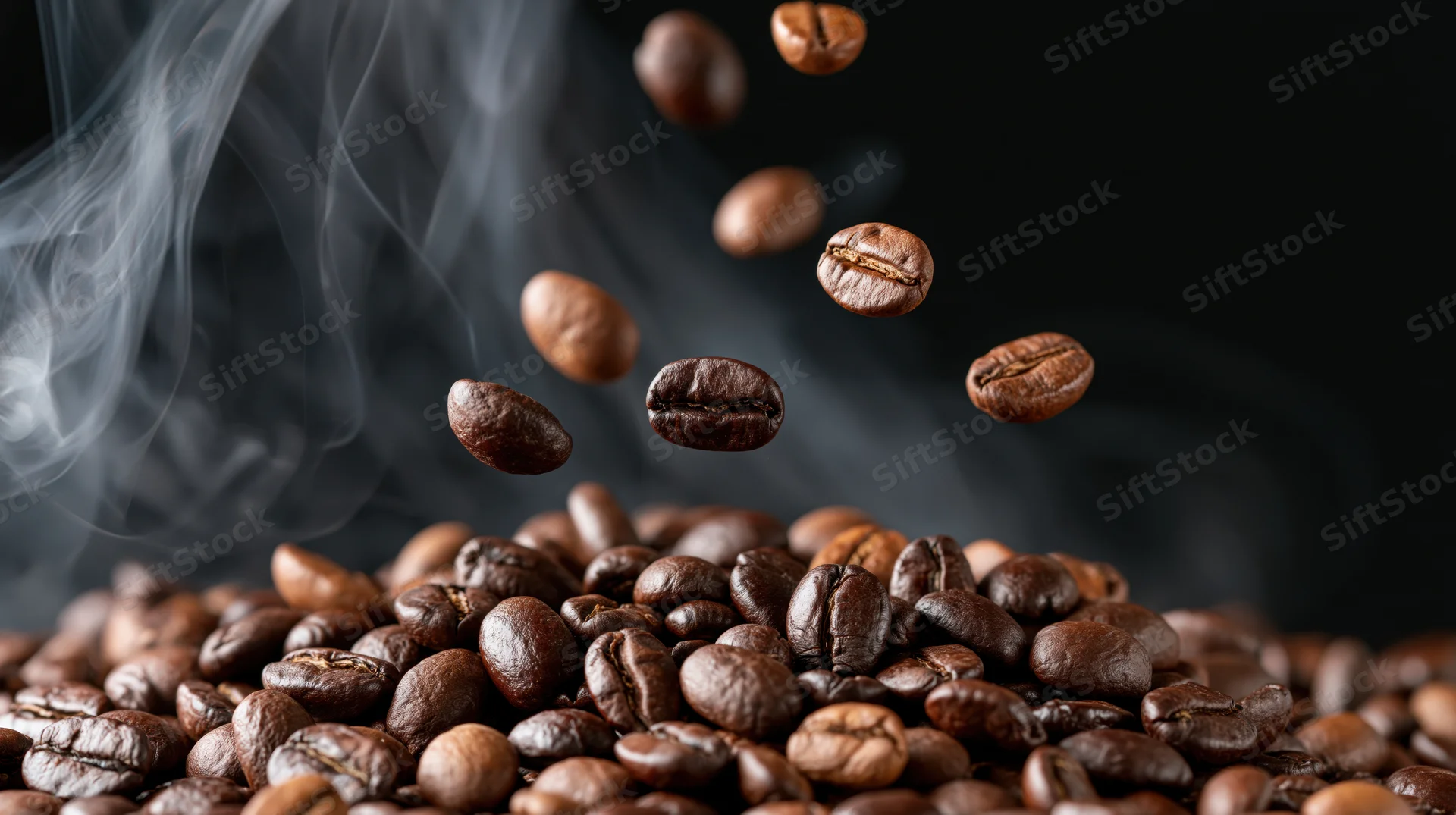 Roasted coffee beans falling in midair above a pile with rising steam