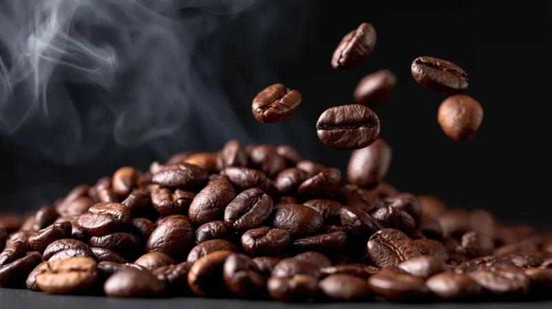 Roasted coffee beans falling and floating above a pile with rising steam on dark background