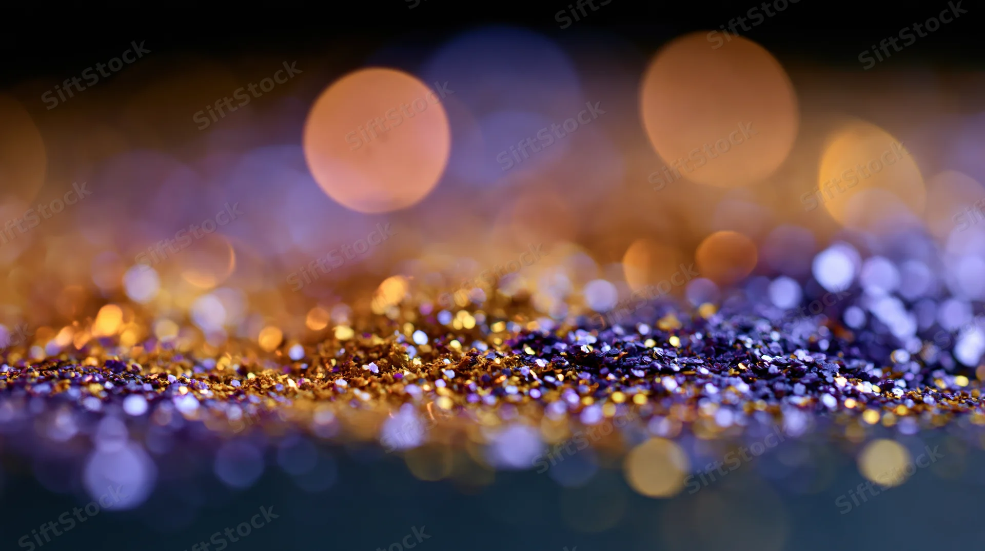 Gold and purple glitter scattered across a dark surface with bokeh lights in the background