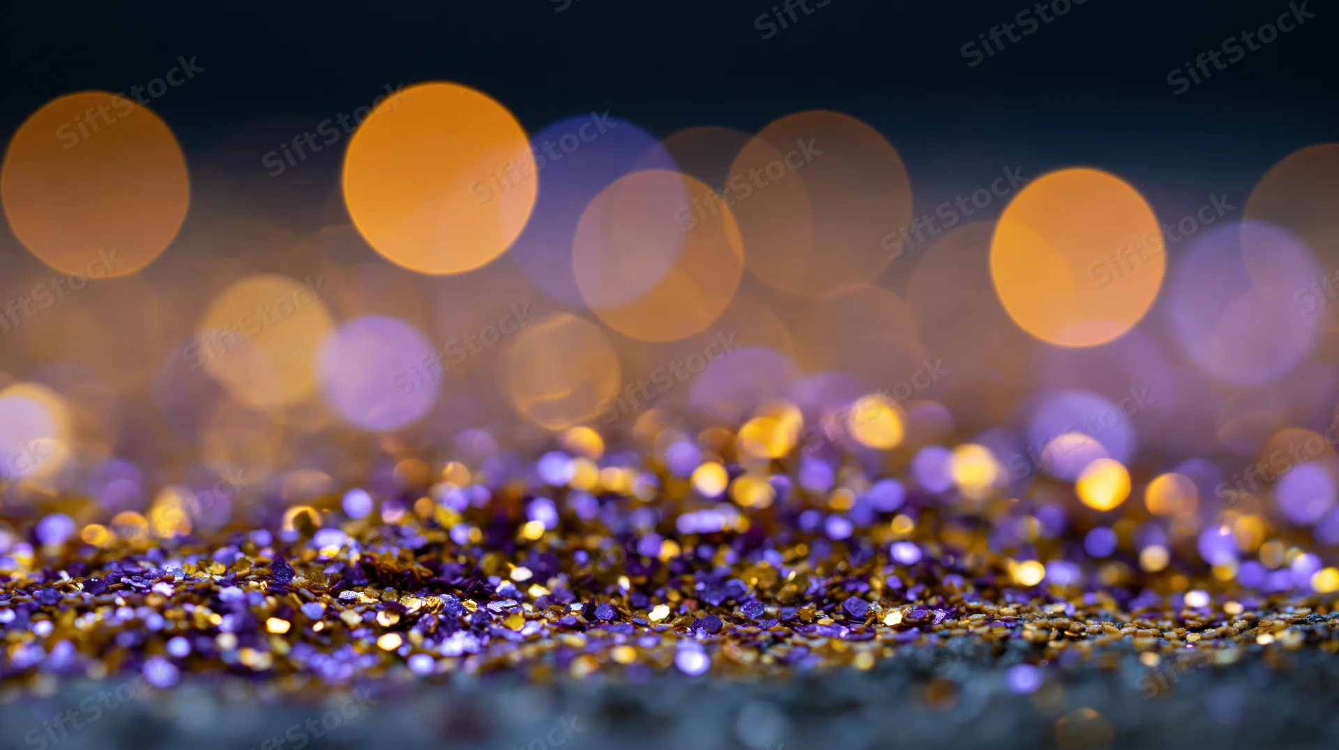 Gold and purple glitter scattered on a dark surface with blurred bokeh lights in the background