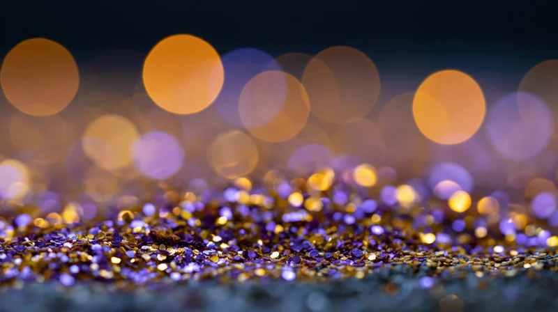 Gold and purple glitter scattered on a dark surface with blurred bokeh lights in the background