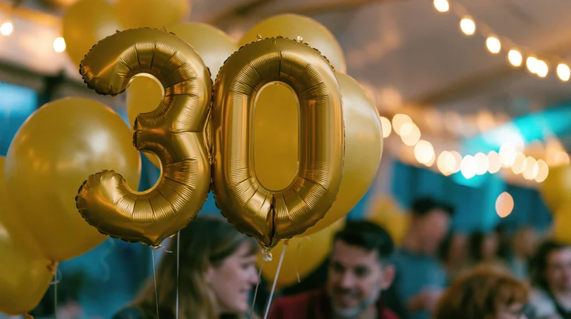Gold foil number 30 balloons floating at a birthday party with people in the background