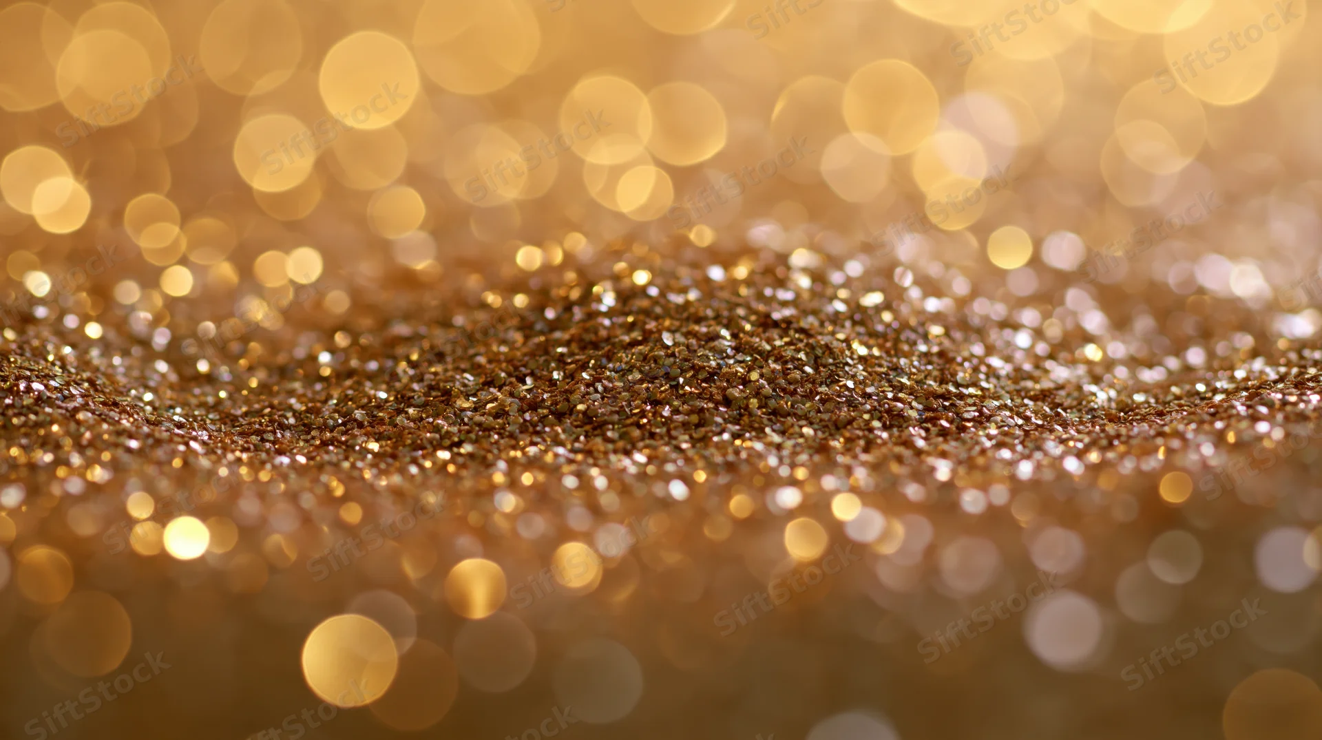 Gold glitter scattered across a flat surface with bokeh lights in the background