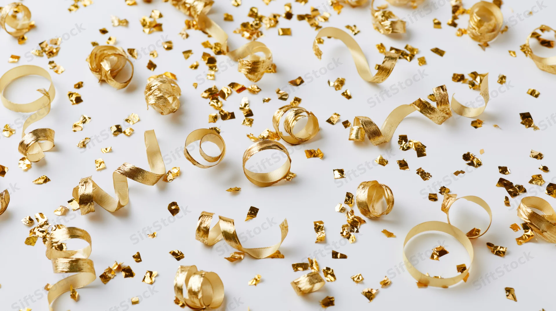Gold confetti and ribbon streamers falling on white surface