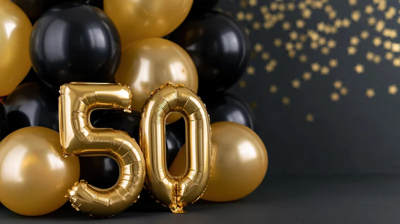 Gold metallic number 50 balloons with black and gold balloons on dark surface, copyspace on right