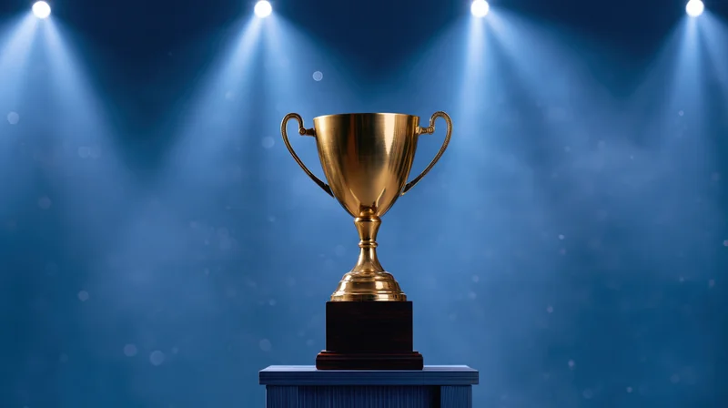 Golden trophy cup on a dark wooden pedestal under spotlights on a stage