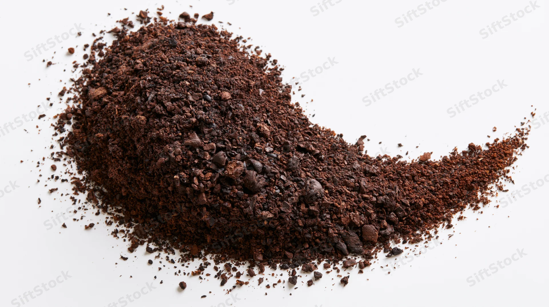 Pile of ground coffee and coarse bean fragments scattered on white surface