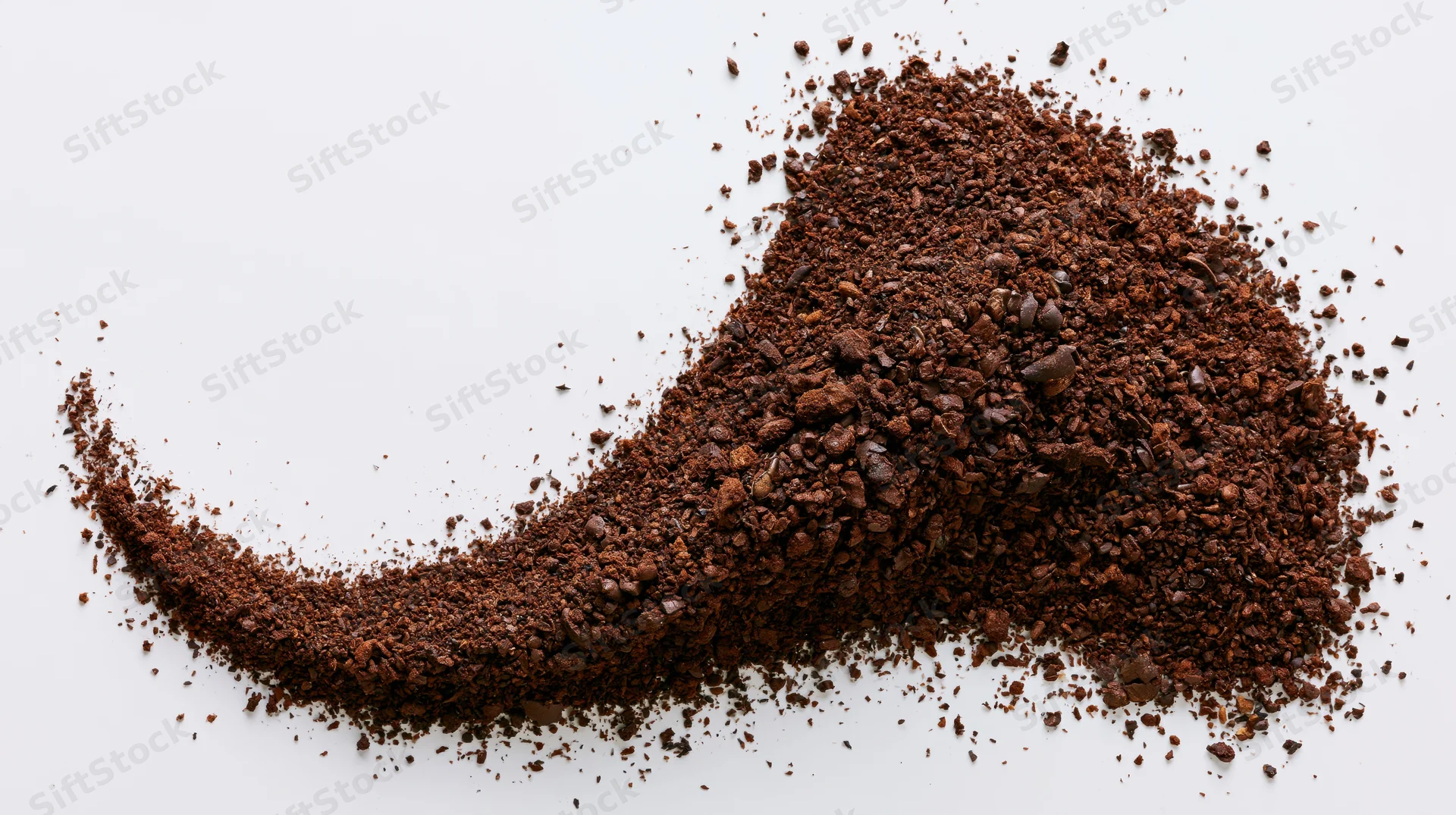 Pile of ground coffee and coarse bean fragments scattered on white surface