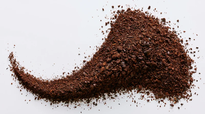 Pile of ground coffee and coarse bean fragments scattered on white surface